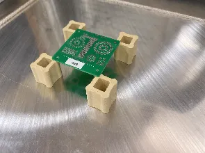 A PCB elevated on four ceramic standoffs on the hotplate for full-convection reflow